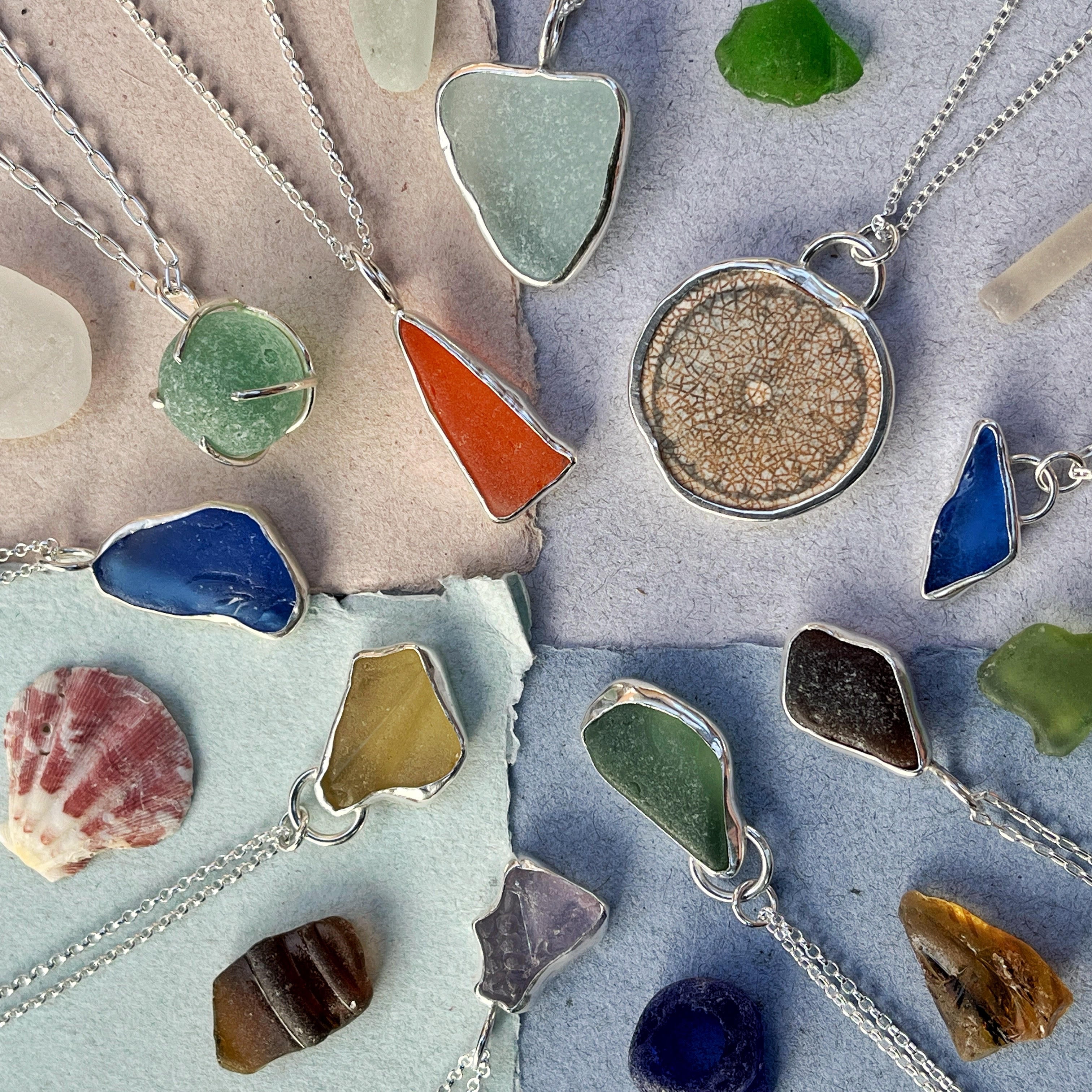 a colourful flatlay of seagglss and pottery scraps, set in silver and laid out with shells